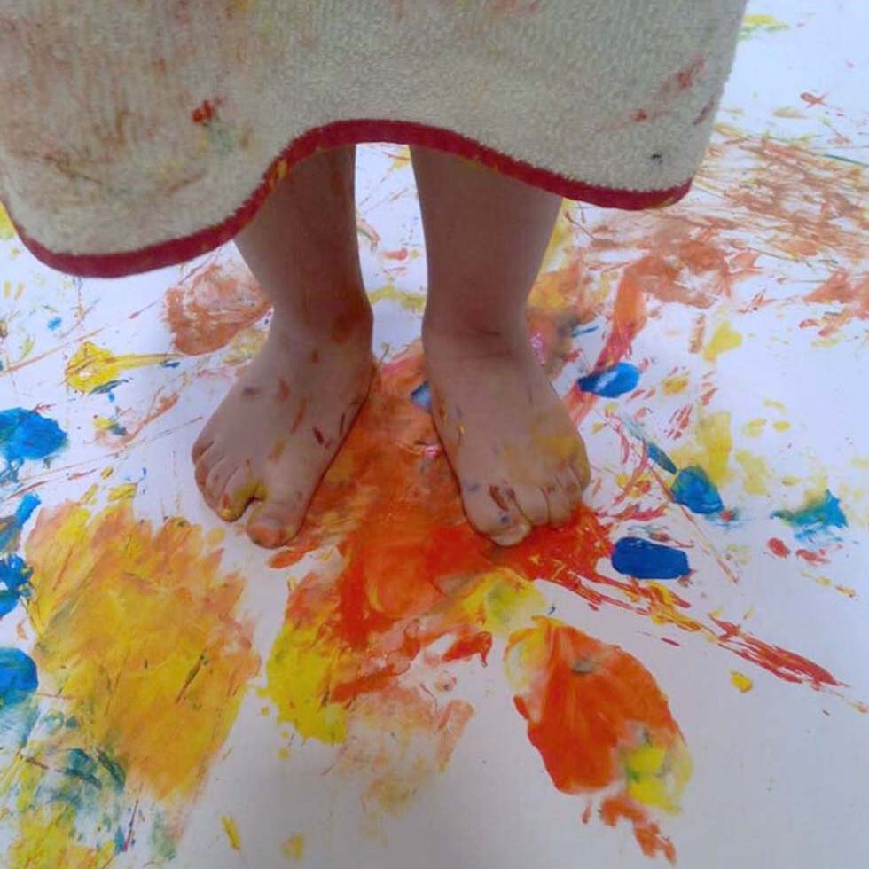 Photos d'un enfant debout sur une feuille peinte avec les pieds lors d'une activité à la crèche Krysalis